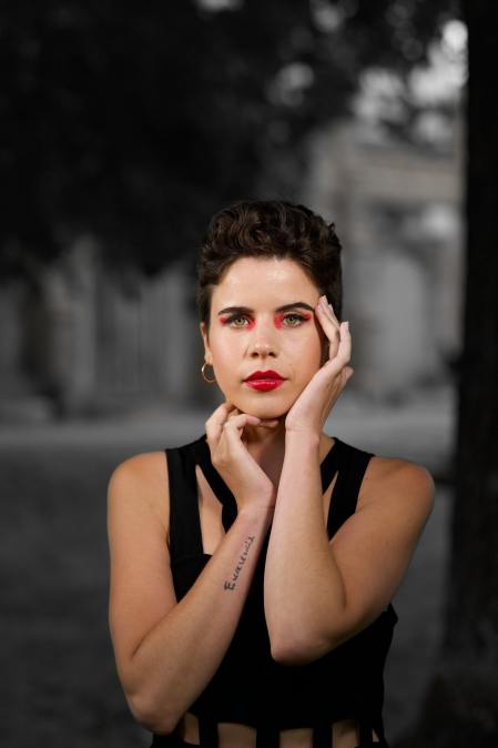 Mujer tiene sus manos rodeando su cabeza. En su antebrazo derecho se ve un pequeño tatuaje con la palabra "Excelencia".