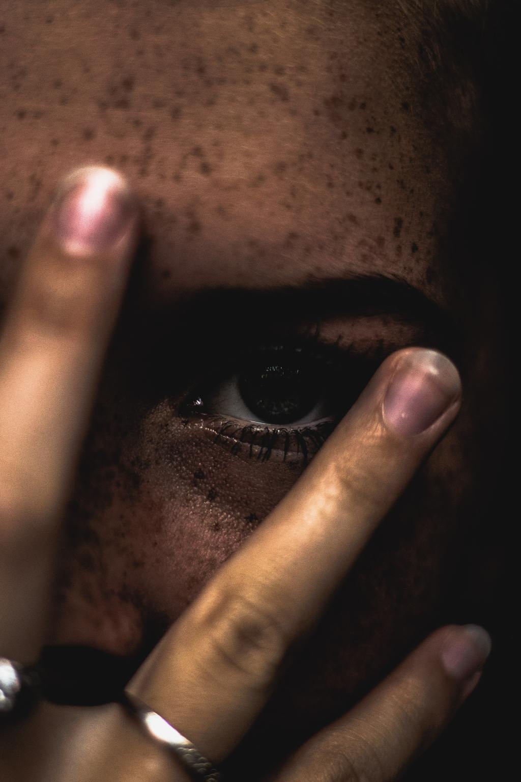 Una mujer tapa su cara y solo deja ver parte de su ojo, como si se estuviera escondiendo.