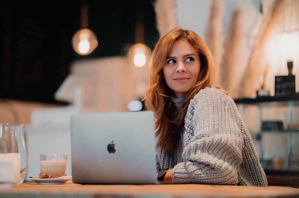 Mujer está sentada frente a una computadora, mira hacia un lado, pícara.