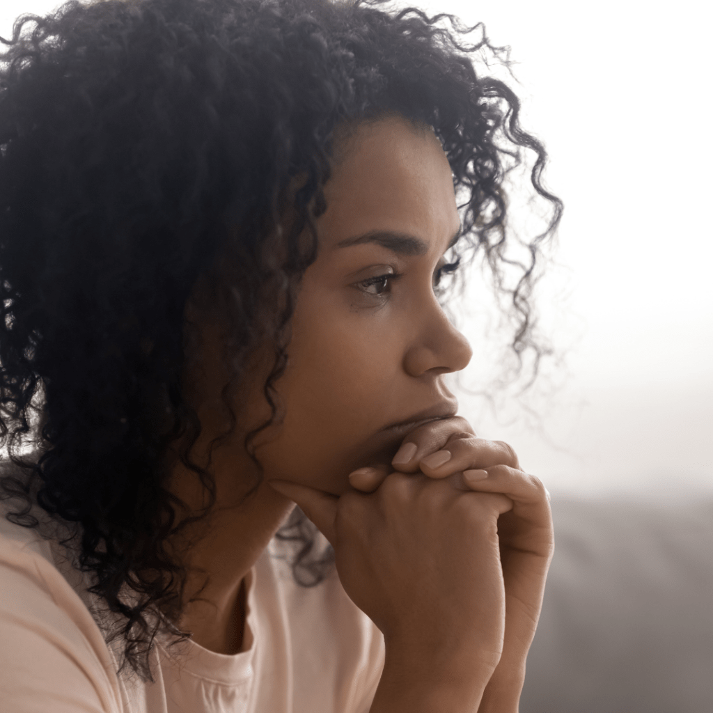 Mujer pensativa mira hacia el horizonte reposando su mentón en sus dos manos.