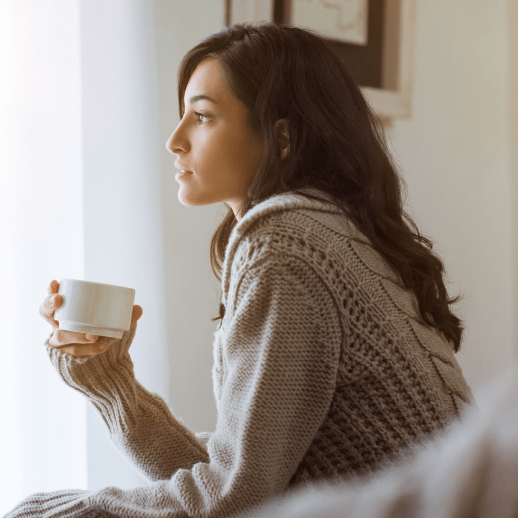 Mujer sostiene taza de café y ve al horizonte, pensativa.
