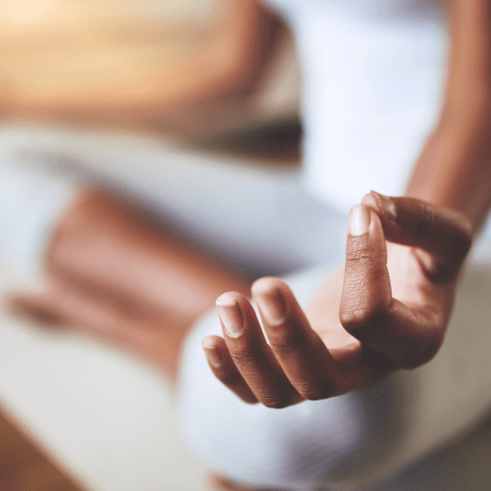 El cuerpo de una mujer en la postura de flor de loto. Se ve de cerca su mano en posición para meditar.