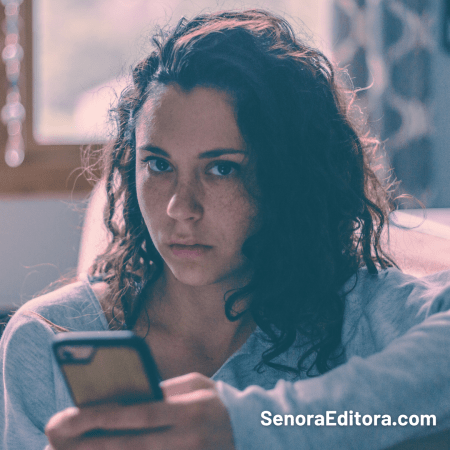 Mujer sostiene un teléfono con su mano izquierda y mira a la cámara molesta.