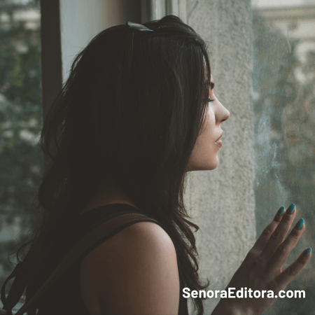 Una mujer mira hacia la ventana, sostiene su mano en la ventana, tiene una mirada nostálgica.
