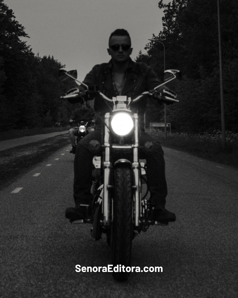 Una persona conduce una motocicleta con el faro encendido. Es una imagen dramática en blanco y negro.