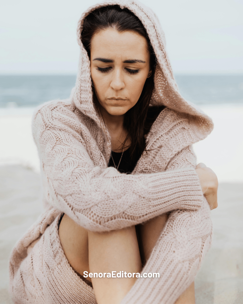 Mujer, melancólica, está sentada en la playa, dándole la espalda al mar